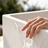 A hand gently touching a smooth, modern bathtub with water droplets, surrounded by a natural outdoor setting.