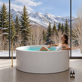 A woman relaxing in a round white bathtub with mountains and trees in the background.
