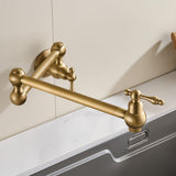 A brushed gold wall-mounted folding faucet with a long articulated arm and lever handle over a sink.