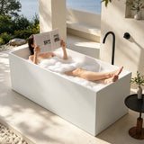 A woman relaxing in a modern bathtub filled with bubbles in a serene outdoor setting.
