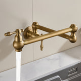 Antique brushed brass wall-mounted pot filler faucet with dual handles and a smooth curved spout dispensing water against a backsplash and countertop