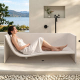 A woman relaxing in a modern bathtub placed outdoors with a scenic view.