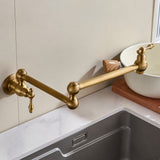 A gold-colored folding kitchen faucet mounted on a wall beside a sink, shown in a studio-like setting