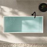 A top-down view of a modern bathtub with a light blue interior, surrounded by pebbles and a plant.