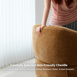 Hand resting on the rounded back of a mustard-brown upholstered barrel chair by sheer curtains