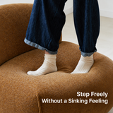 Close-up of white socks standing on the rust-brown chenille seat of a swivel barrel chair, pressing into the cushion