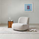 Light beige swivel barrel chair on a rug in a bare room with a wooden side table and blue-red artwork