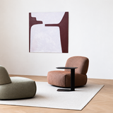 Rust-brown swivel barrel chair and black side table on a light rug in a bright room