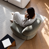 Woman lounging in a gray-green chenille swivel barrel chair on a rug, viewed from above