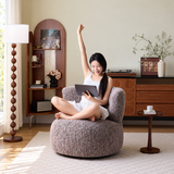 Woman with tablet sitting cross-legged on a brown mottled swivel barrel chair in a warm living room