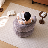 Overhead view of a woman reading in a mottled lilac swivel barrel chair on a cream rug