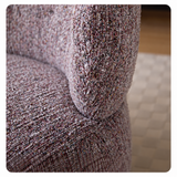 Close-up of mottled loop yarn upholstery on a swivel barrel chair seat and curved backrest, blurry rug behind