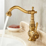 Brass vintage kitchen faucet with floral engravings, curved spout, and side lever, displayed on a marble countertop.