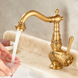 Brass vintage kitchen faucet with floral engravings, curved spout, and side lever, with water flowing on a marble countertop.