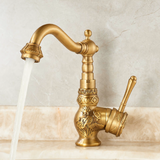 Vintage brass kitchen faucet with floral engravings, curved spout, and side lever, featured on a light marble countertop.