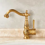 Brass vintage kitchen faucet with floral engravings, curved spout, and side lever on a beige marble countertop.