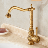 Brass vintage kitchen faucet with floral engravings, curved spout, and a side lever on a beige marble countertop.