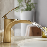 Brushed gold single-handle faucet with a curved spout on a beige countertop, water flowing into a sink.