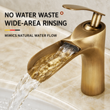 Brushed gold kitchen faucet close-up, water flowing over the open channel spout onto a beige countertop.
