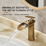 Antique brass single-handle faucet pouring a wide waterfall flow over a beige marble sink, round mirror above.