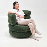 Woman in a white shirt reclining in a green bouclé swivel barrel chair on a white studio backdrop