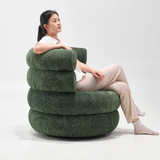 Woman seated in a green bouclé swivel barrel chair with stacked rounded segments, side view on white