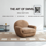 Brown textured barrel chair on a checkered rug in a bright white room with a black side table and framed print