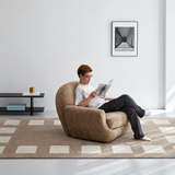 Reader seated in brown textured swivel barrel chair on checkered rug in bright room