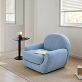 Light blue swivel barrel chair with a book on its seat near a black side table