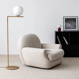 Beige textured swivel barrel chair in a bright minimalist room beside a brass floor lamp and black shelving unit
