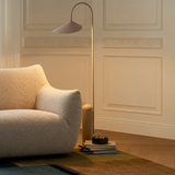 Off-white bouclé swivel barrel chair side view beside an arc floor lamp and stacked books in a warm paneled room
