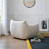 Rear view of a cream textured swivel barrel chair in a white paneled room with herringbone wood floor and colorful rug