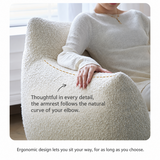 Close-up of an arm resting on a cream bouclé swivel barrel chair's curved armrest