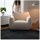 Woman standing behind a cream bouclé swivel barrel chair on a dark rug in a paneled room