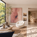 Cream bouclé swivel barrel chair with pillow on a jute rug, pink abstract art and dining area beyond