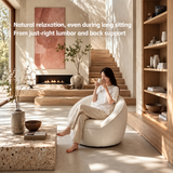 Woman sipping from a mug in a cream bouclé swivel barrel chair, terrazzo coffee table and wood stairs behind