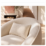 Cream bouclé swivel barrel chair close-up: backrest, lumbar pillow and piped seam, fireplace behind