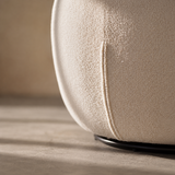 Close-up of cream bouclé barrel chair lower side seam meeting the black base ring on a sunlit floor