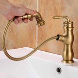 Brushed brass kitchen faucet, hand pulling out the spray head on its coiled hose above a white sink.