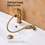 Antique brass pull-out kitchen faucet with coiled hose extended over white sink, mottled tan wall behind
