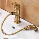Brushed brass kitchen faucet with carved lever handle, pull-out spray head resting in a white sink.