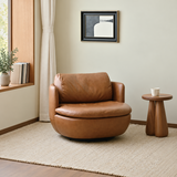 Tan leather-look swivel barrel chair on a cream rug beside a wood side table in a neutral room