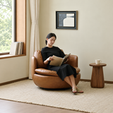 Woman reading in a tan leather-look swivel barrel chair by a window and wood side table