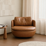 Brown leather-look swivel barrel chair by sheer cream curtains and a round wood side table