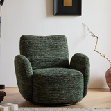 Green textured swivel barrel chair with rounded arms on a wood floor, a dried branch in a vase and black framed art nearby