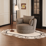 Taupe speckled swivel barrel chair with two cushions on a floral rug by a floor lamp in a panelled room