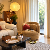 Tan textured swivel barrel chair with red heart cushion in a sunlit living room beside a coffee table and white sofa