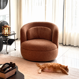 Rust-brown swivel barrel chair on a pale rug with an orange cat lying beside it, sheer curtains behind