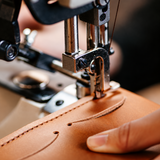 Sewing machine needle stitching tan upholstery fabric with a curved seam, close-up detail
