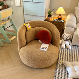 Textured tan swivel barrel chair in a living room with a red fluffy cushion, toys, and a black-and-white rug